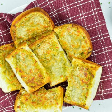 pieces of garlic bread cut from a loaf, set in a bowl, with schezwan chutney dip on the side