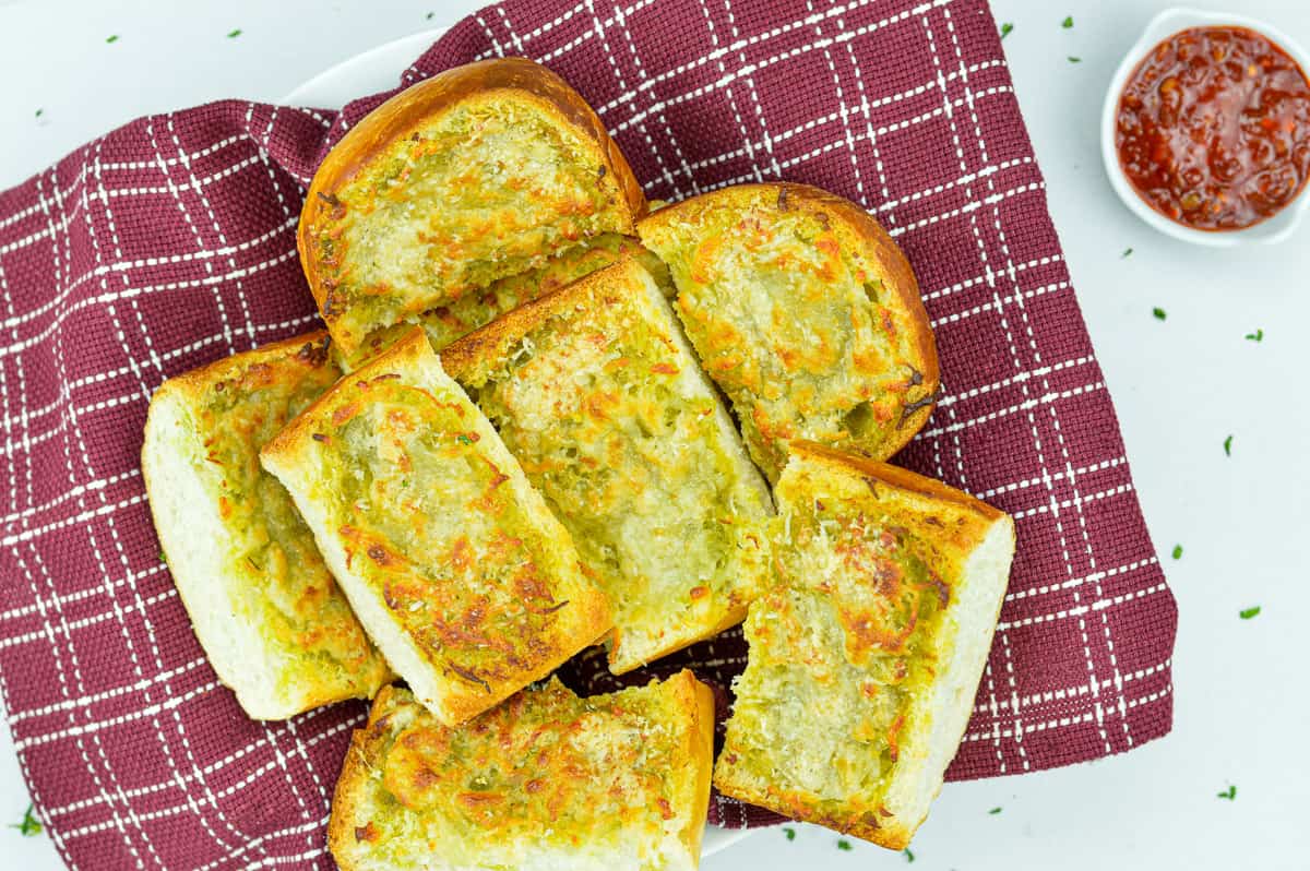 pieces of garlic bread cut from a loaf, set in a bowl, with schezwan chutney dip on the side