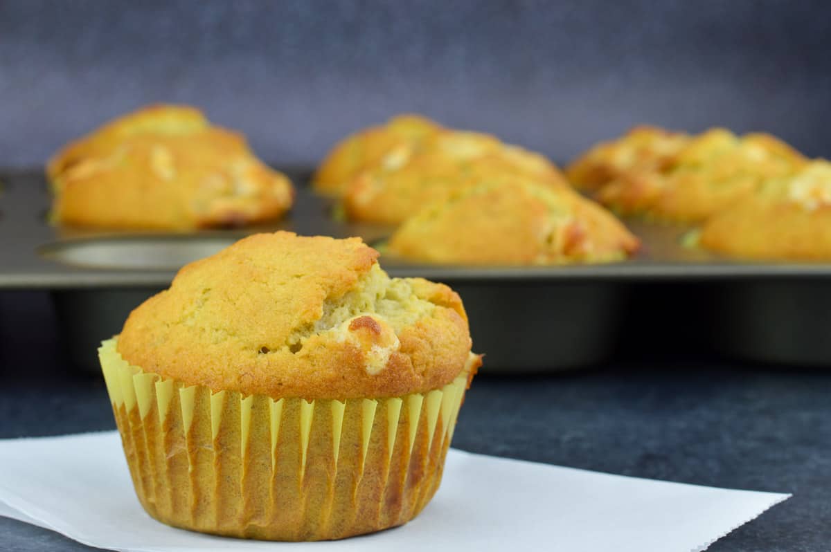 a banana white chocolate chip muffin placed in the front of a tray full of more muffins in the background