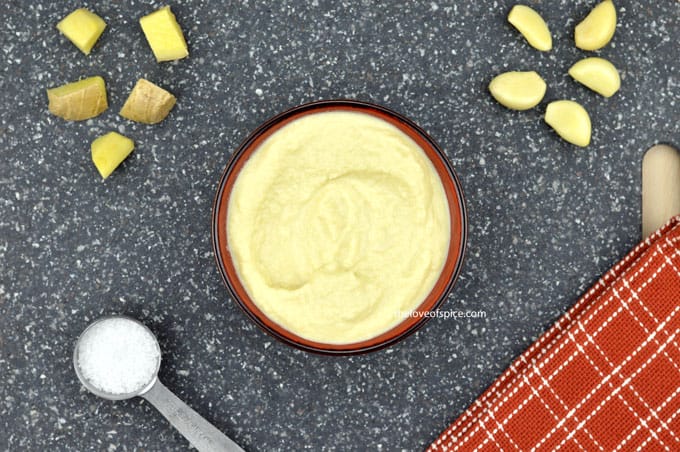 ginger garlic paste in a red bowl, along with some chunks of ginger & garlic, and some salt