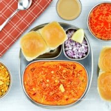 a plate of kolhapuri misal pav served with chopped onions, farsan, tari and tea