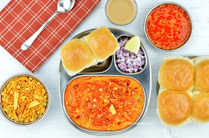 a plate of kolhapuri misal pav served with chopped onions, farsan, tari and tea