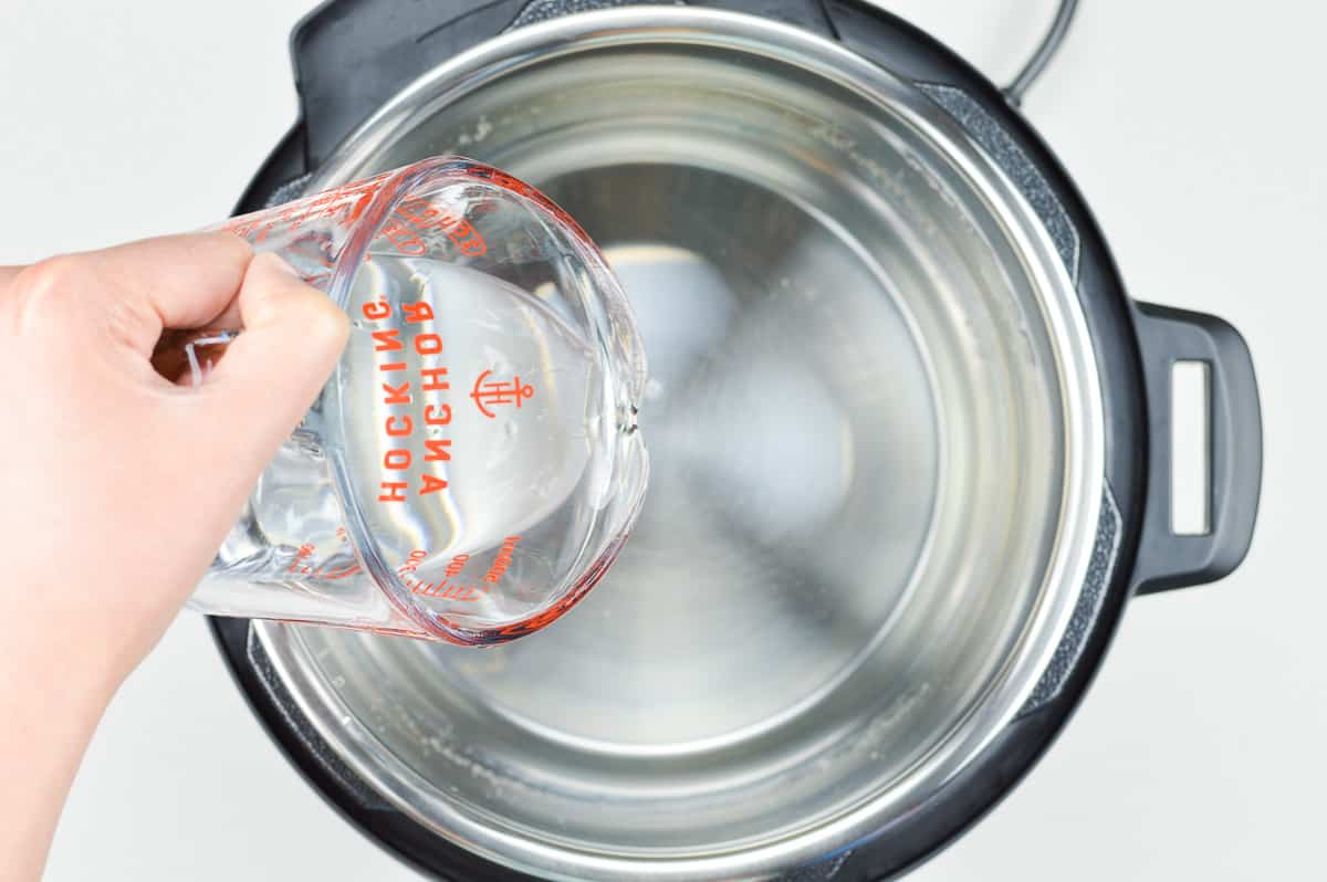 hand pouring water from a measuring jug into the inner pot of the instant pot