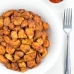 indian spiced air fryer chicken bites served in a white bowl, with a fork and dipping sauce on the side