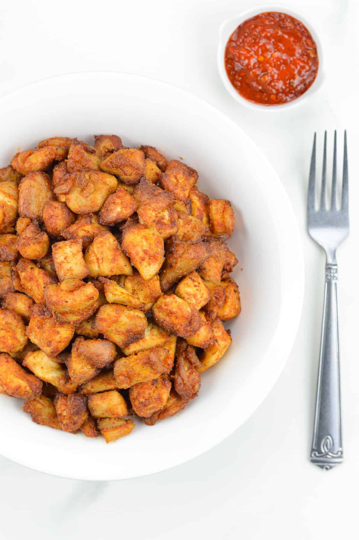 indian spiced air fryer chicken bites served in a white bowl, with a fork and dipping sauce on the side