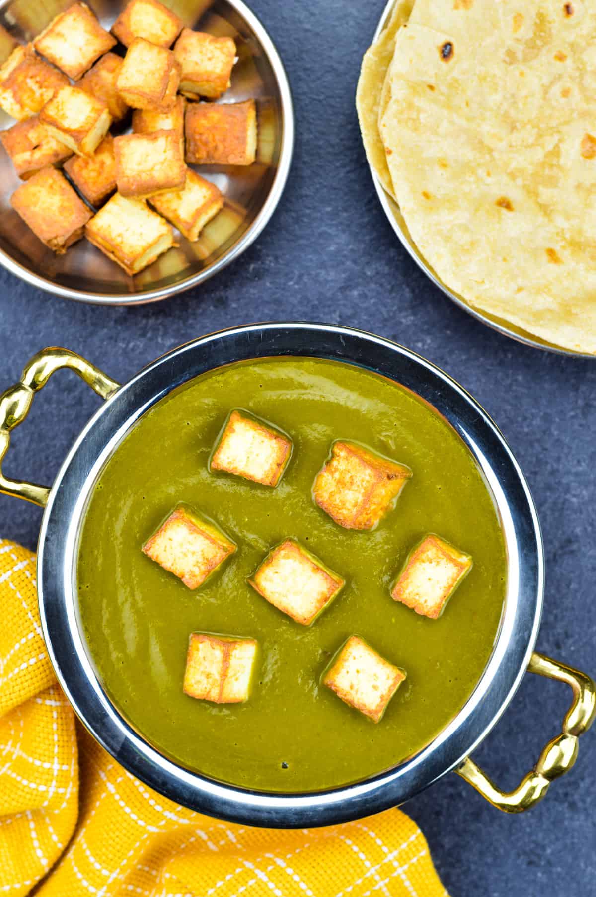 palak paneer in traditional indian serving kadai, with homemade chapatis, and extra pan fried paneer cubes on the side