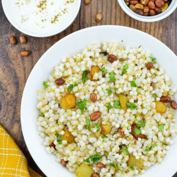 a plate full of sabudana khichdi, with a bowl of roasted peanuts, and a bowl of yogurt on the side