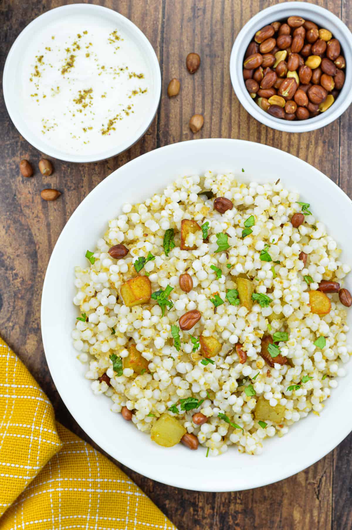 a plate full of sabudana khichdi, with a bowl of roasted peanuts, and a bowl of yogurt on the side