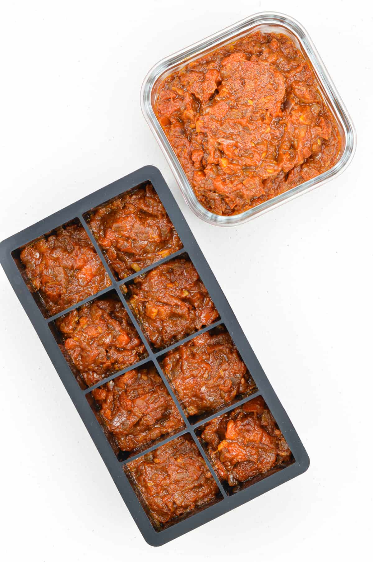 bhuna masala curry sauce base portioned out in a black ice cube tray and also in a glass storage container