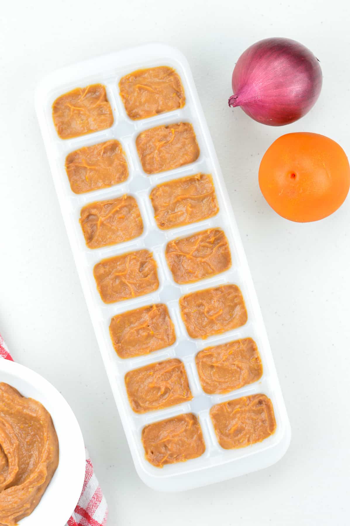 onion tomato masala paste filled in an ice cube tray, with some more paste in a bowl on one side, and a raw onion and tomato on the other side