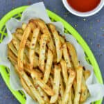 air fried french fries in a green fast food serving basket, with a small bowl of ketchup on the side