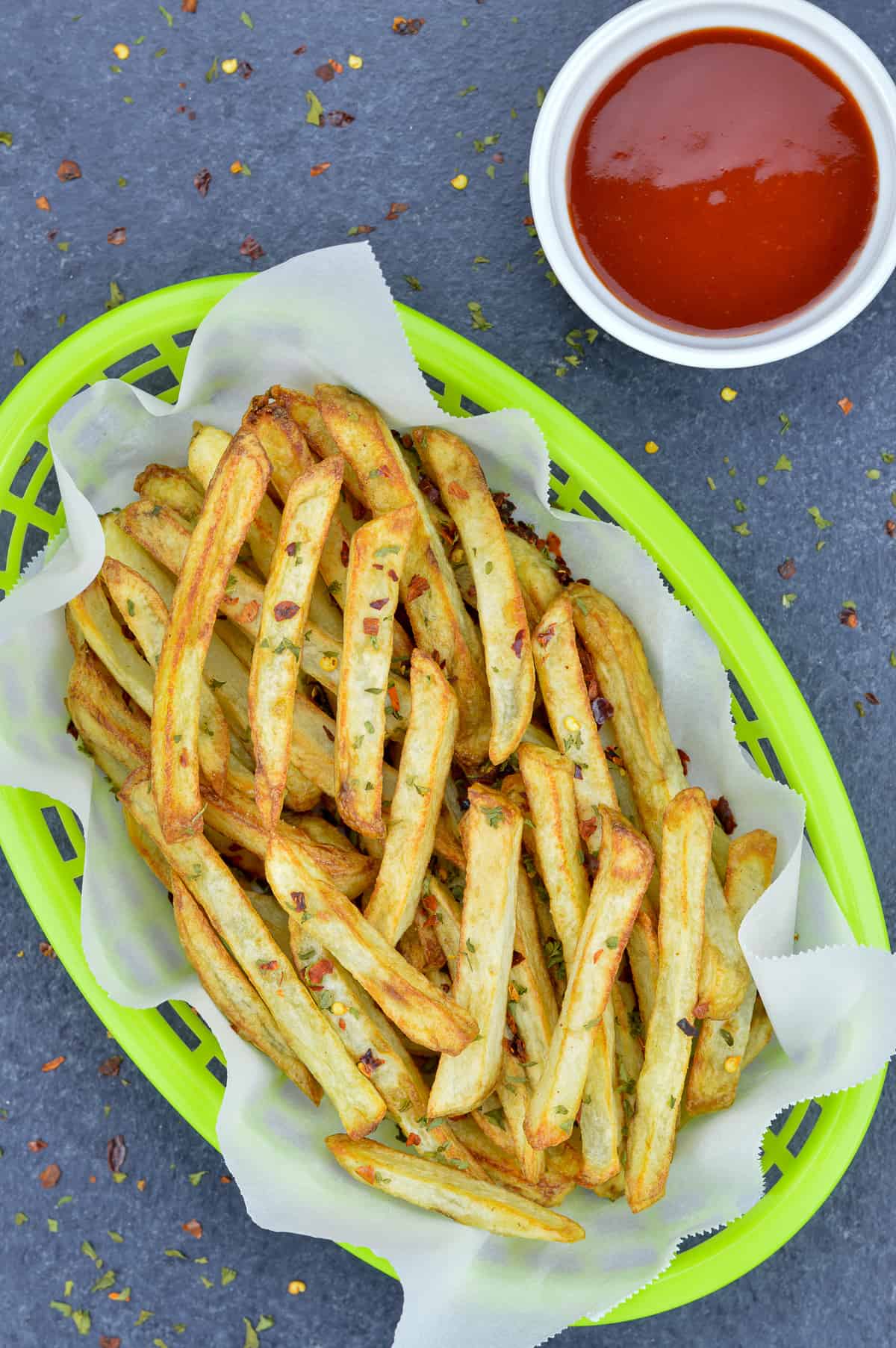 air fried french fries in a green fast food serving basket, with a small bowl of ketchup on the side
