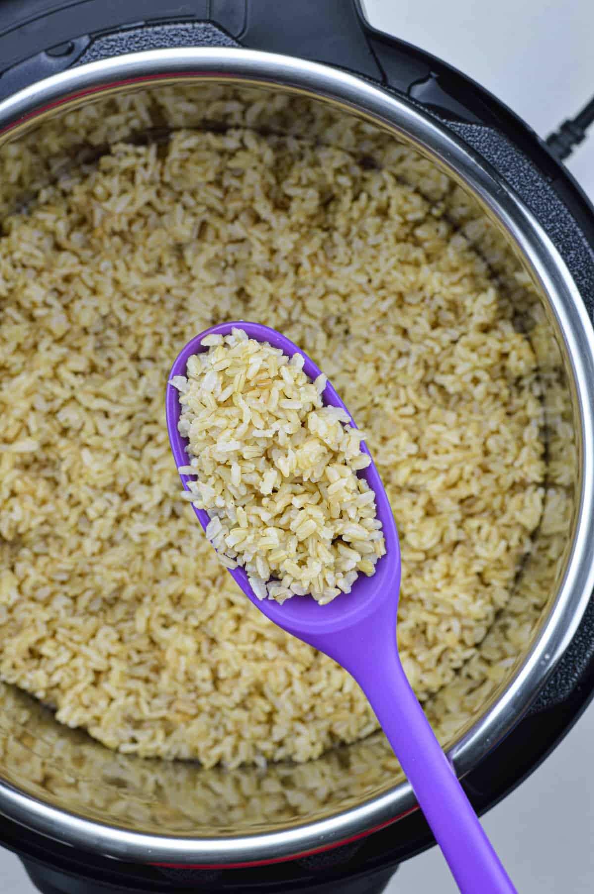 a small quantity of cooked brown rice in a ladle, held above an instant pot full of cooked brown rice