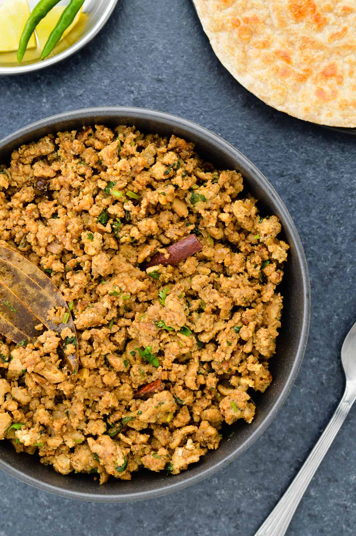 a big bowl full of chicken keema, served with rotis, a few green chillies & lemon wedges on the side