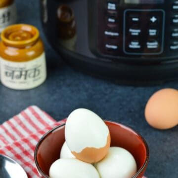 a bowl of hard boiled eggs, with one egg half peeled, along with mealthy multipot 2.0, an unpeeled egg, and salt & pepper shakers in the background