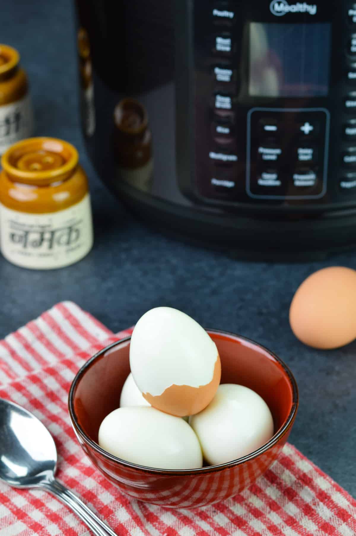 a bowl of hard boiled eggs, with one egg half peeled, along with mealthy multipot 2.0, an unpeeled egg, and salt & pepper shakers in the background