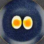 a blue plate with one soft boiled egg, which is cut open vertically into two