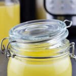 Instant Pot ghee in a small glass jar, and another bottle of ghee & Instant Pot in the background
