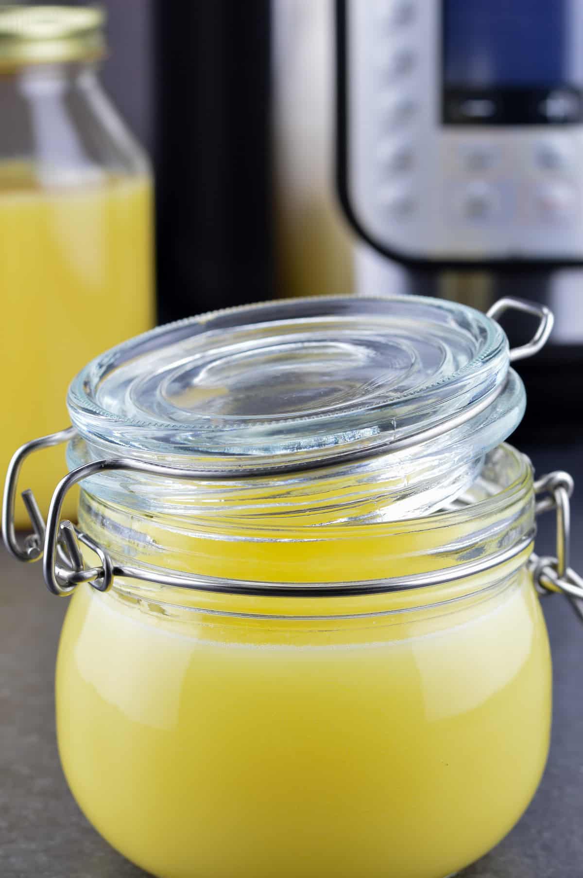 Instant Pot ghee in a small glass jar, and another bottle of ghee & Instant Pot in the background