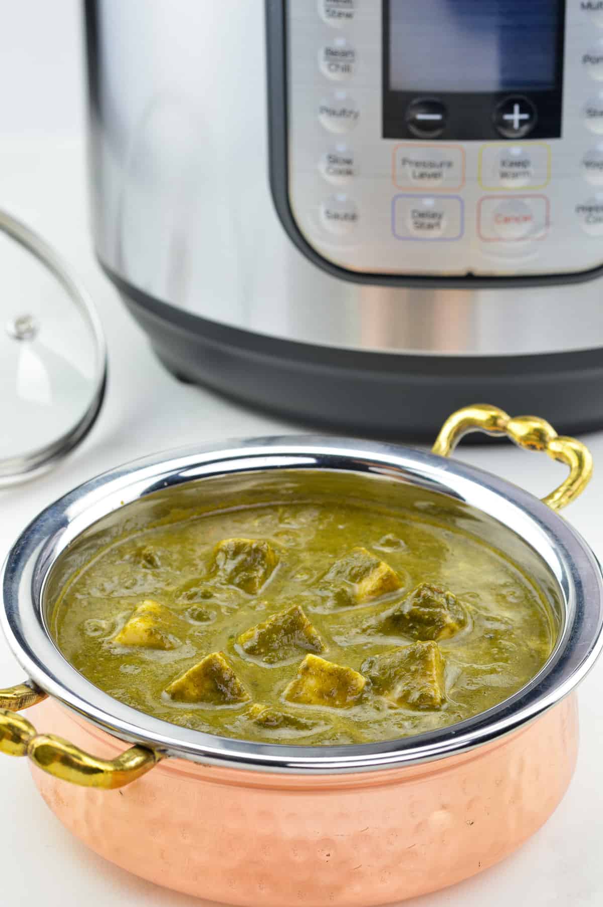 a close up shot of kadai full of palak paneer made in instant pot, with an Instant Pot in the background