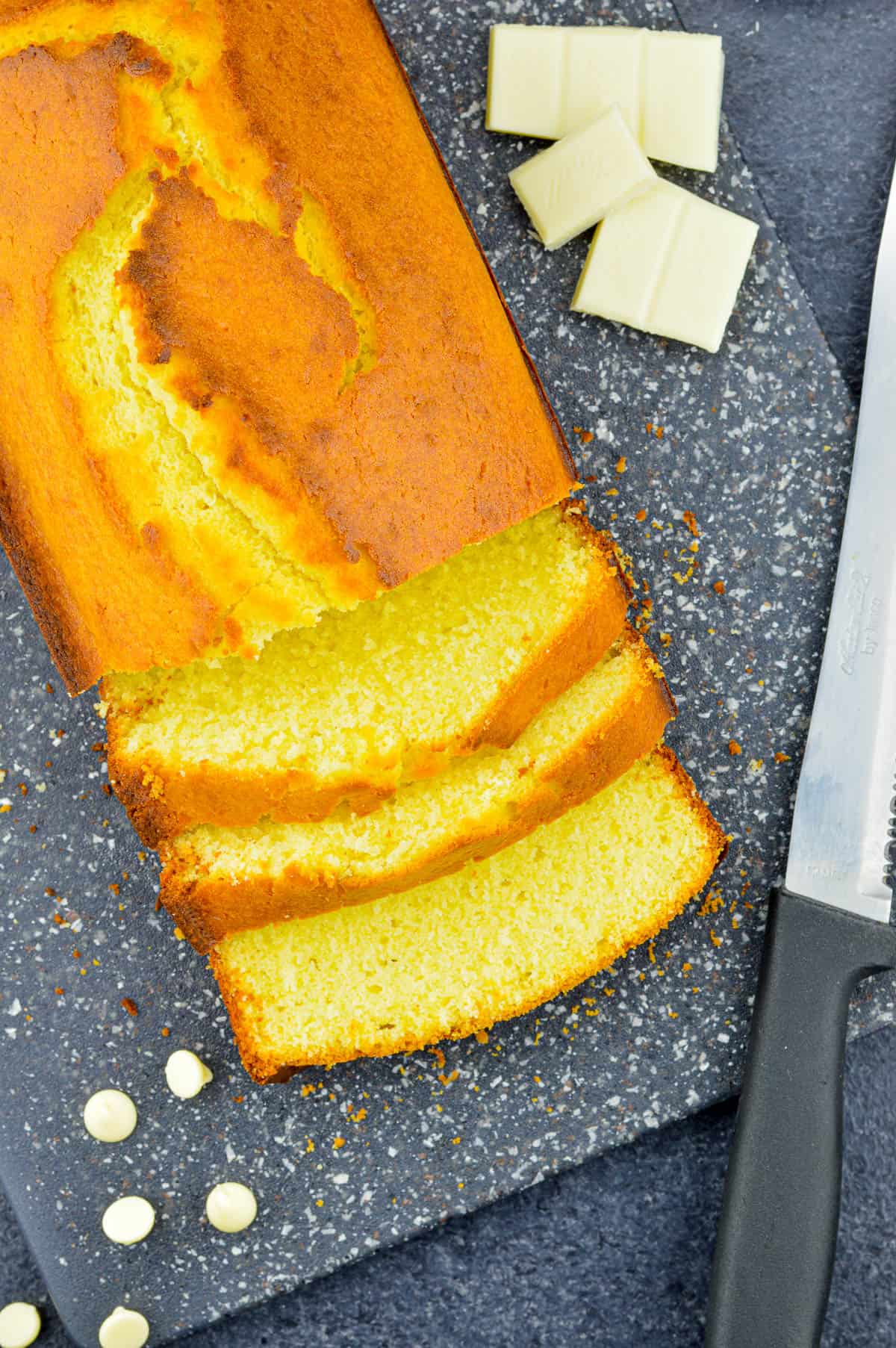 top shot of a loaf of white chocolate pound cake, with a few slices cut from the loaf, and a few pieces of white chocolate bar & chocolate chips on the sides