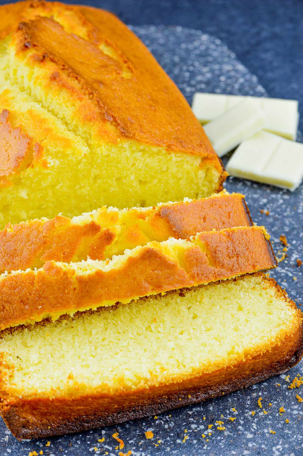 close up of a loaf of white chocolate pound cake, with a few slices cut from the loaf, and a few pieces of white chocolate bar in the background