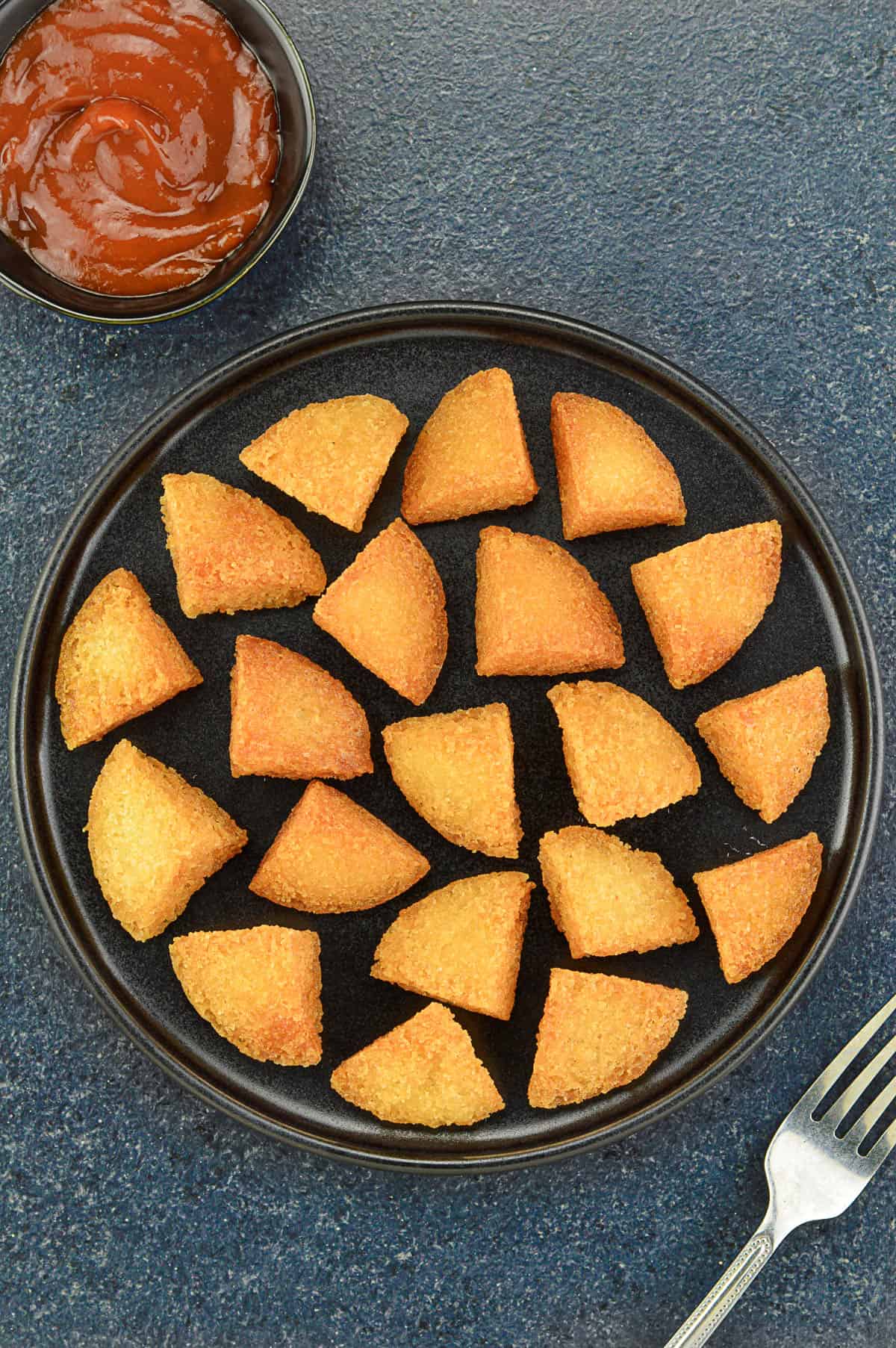 top shot of a plate of crispy deep fried idli bites, served with a schezwan chutney dip on the side
