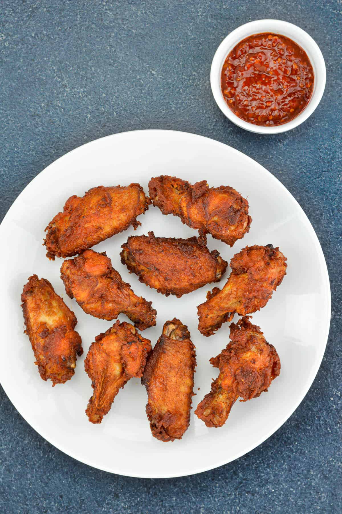 top shot of a plate full of indian spiced fried chicken wings, with a small dipping bowl of schezwan chutney on the side