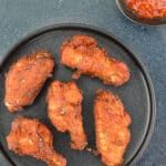 top shot of a plate of indian spiced fried chicken wings, served with a small dip of schezwan chutney on the side