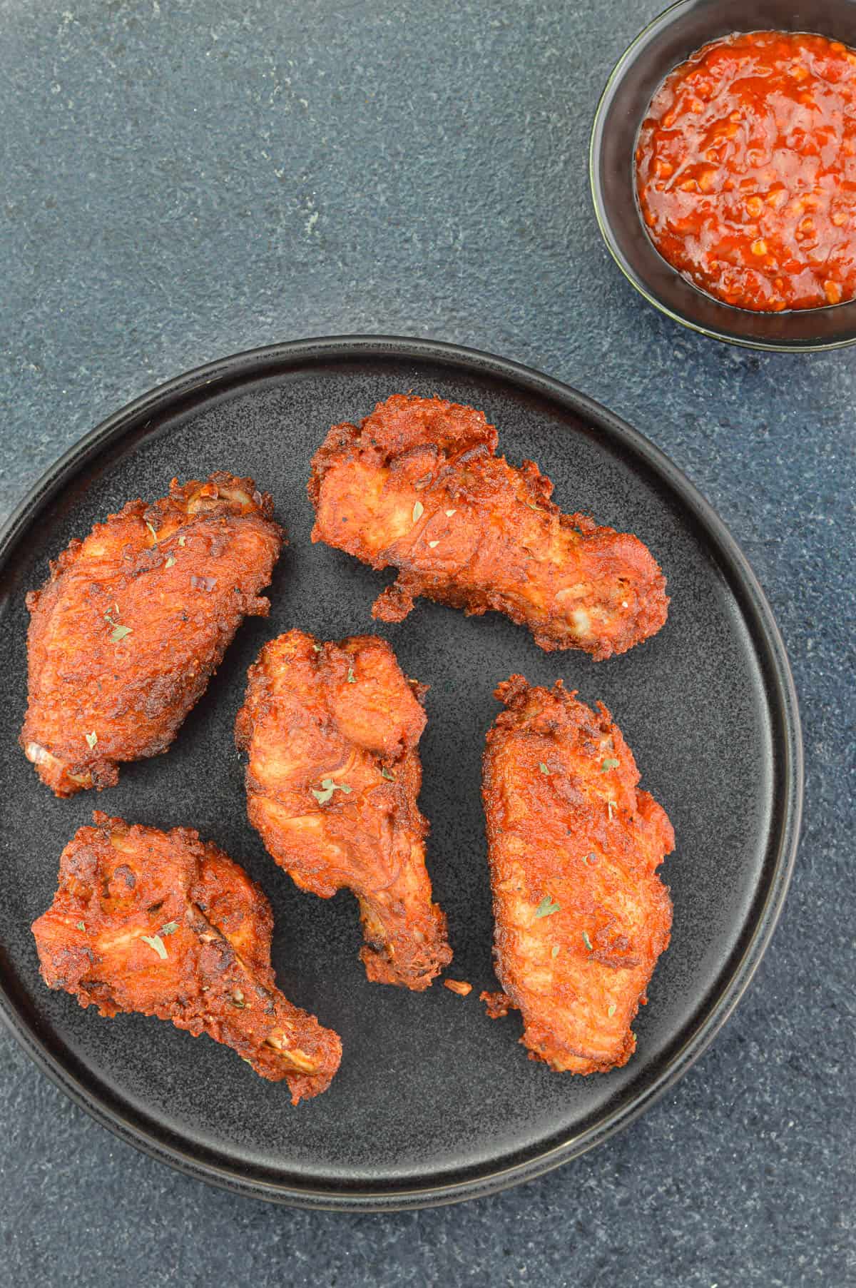 top shot of a plate of indian spiced fried chicken wings, served with a small dip of schezwan chutney on the side