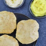 a plate full of puffed puris, served with elaichi shrikhand and pineapple shrikhand on the side