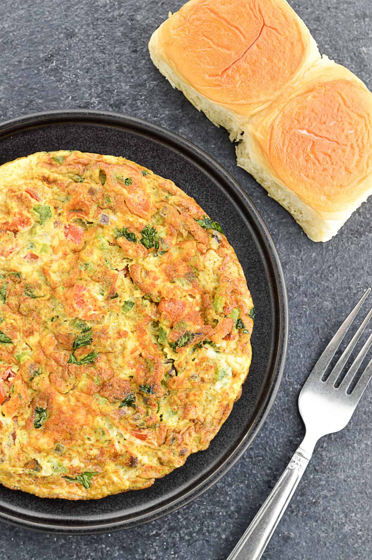 indian style masala omelette served in a plate, with 2 Indian style ladi pav on the side