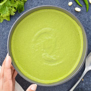 a big bowl of green sandwich chutney, with some of the ingredients to make the chutney laid down next to it