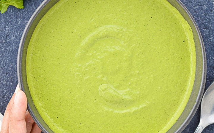 a big bowl of green sandwich chutney, with some of the ingredients to make the chutney laid down next to it