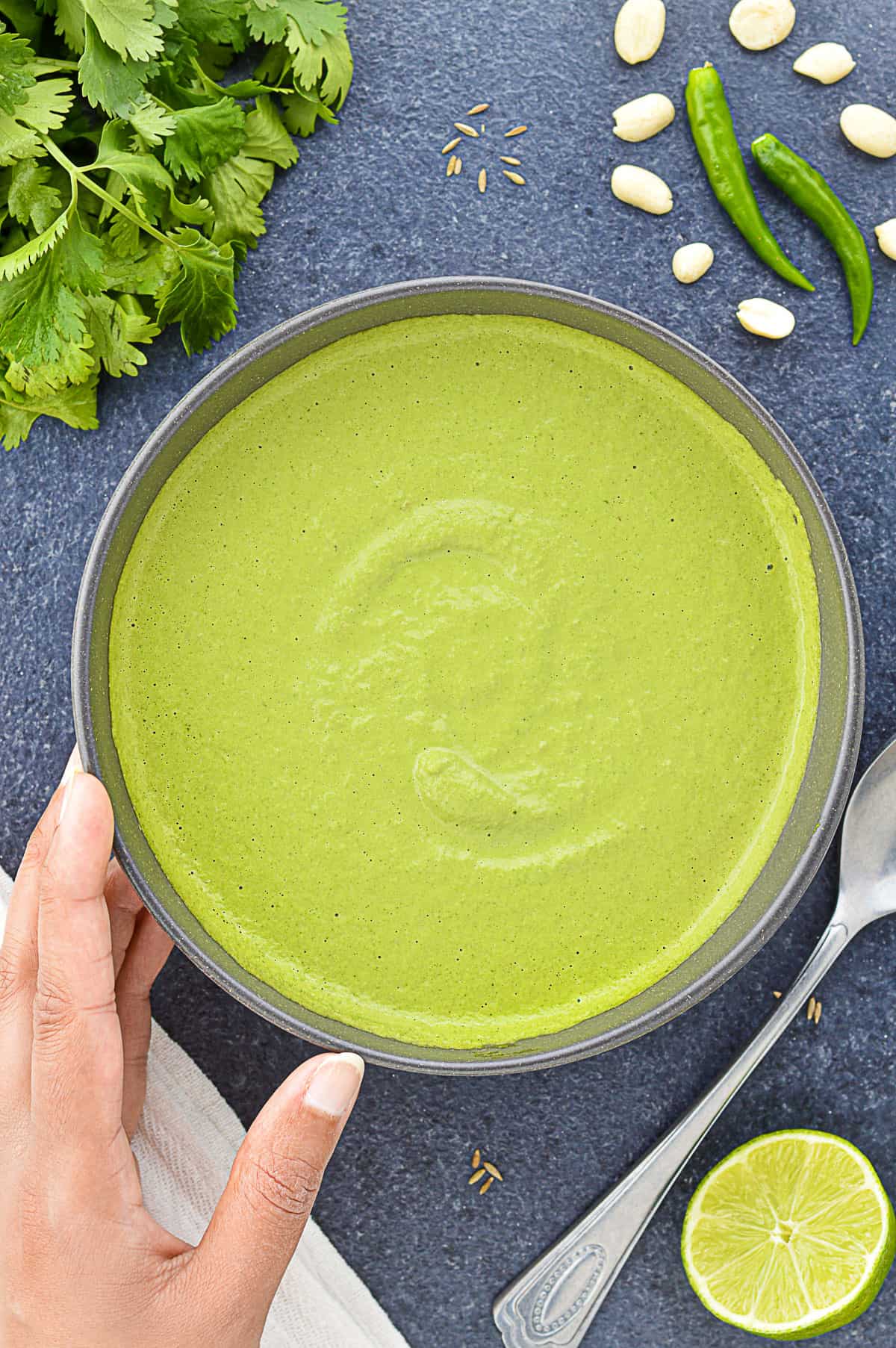 a big bowl of green sandwich chutney, with some of the ingredients to make the chutney laid down next to it