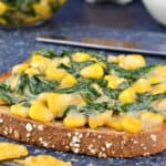 open faced spinach corn sandwich on cuttting board, with additional sandwich filling and tea in the background