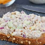 a close up shot of an open faced tuna salad sandwich, with more sandwich filling, and chips in the background