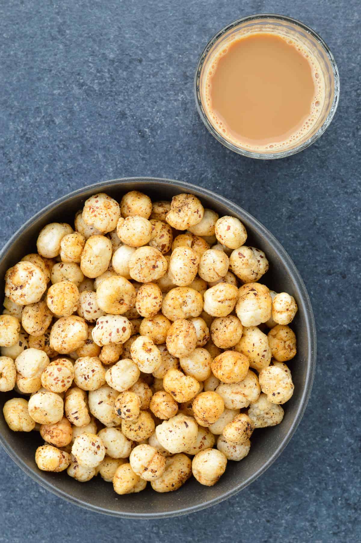 top shot of a bowl full of homemade masala makhana with a glass of tea on the side