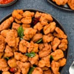 top shot of a plate full of homemade chicken 65, with another serving on the side, along with some schezwan chutney