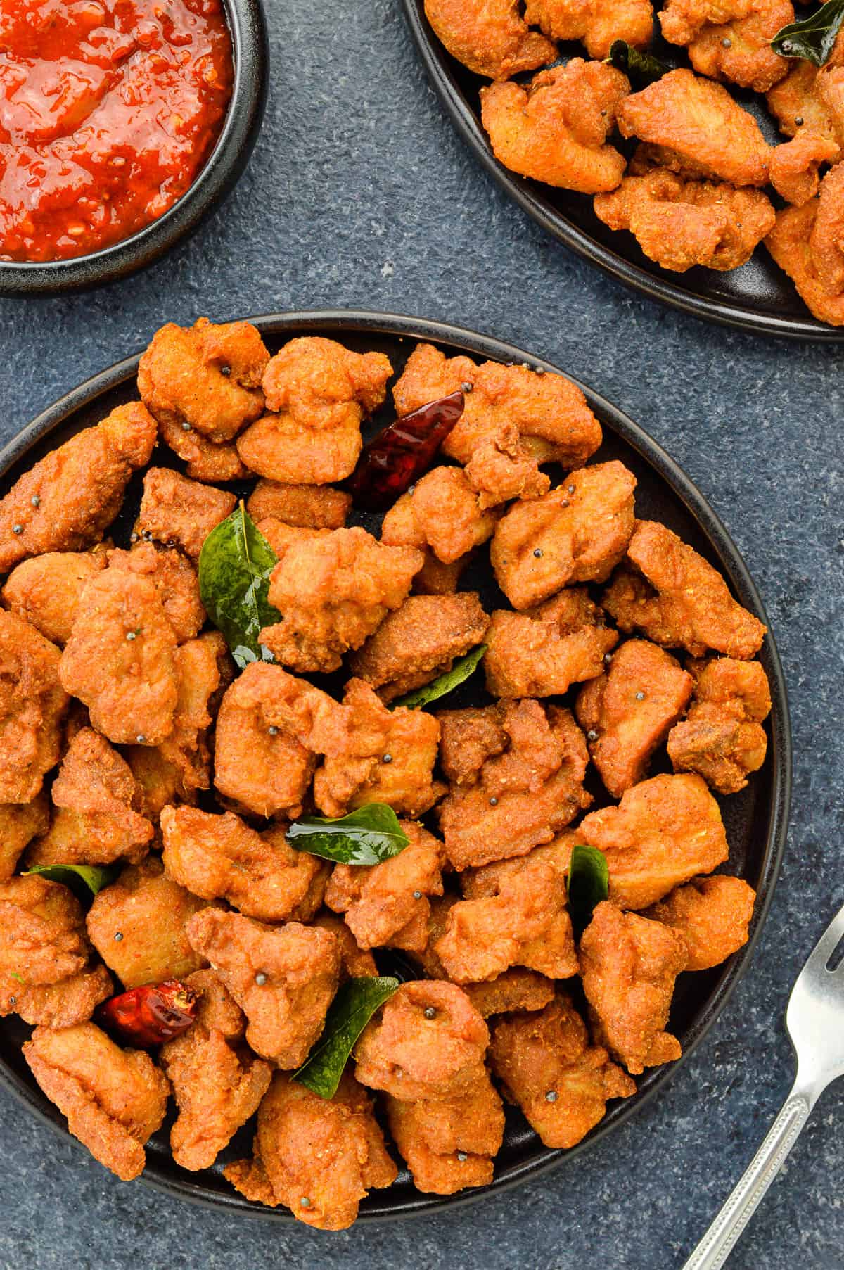 top shot of a plate full of homemade chicken 65, with another serving on the side, along with some schezwan chutney