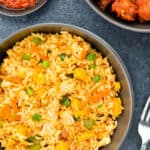 top shot of a bowl full of chicken fried rice, with chicken manchurian and schezwan chutney on the side.