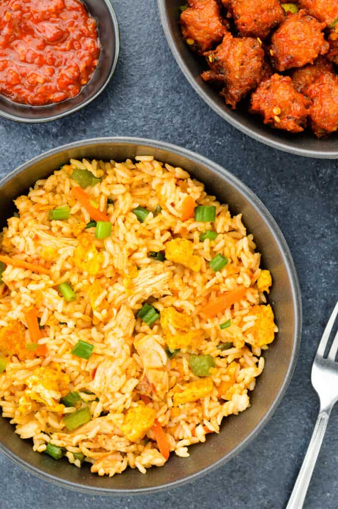 top shot of a bowl full of chicken fried rice, with chicken manchurian and schezwan chutney on the side.