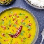 a big bowl full of homestyle dal fry, with a bowl of rice, and a small bowl of green beans stir fry on the side.