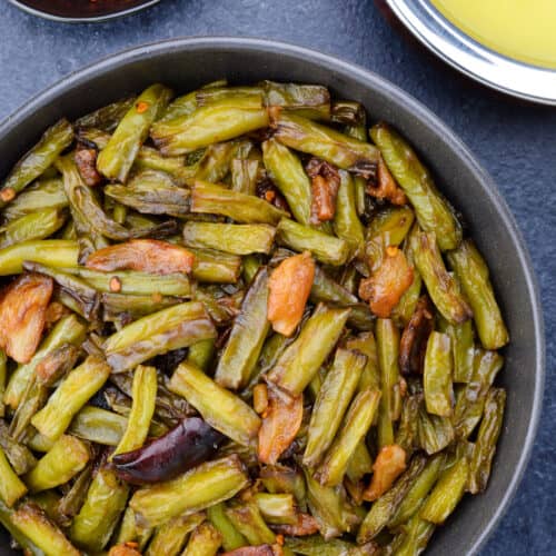 top shot of a bowl full of indian green beans stir fry, with a bowl of dal and red garlic chutney in the background.