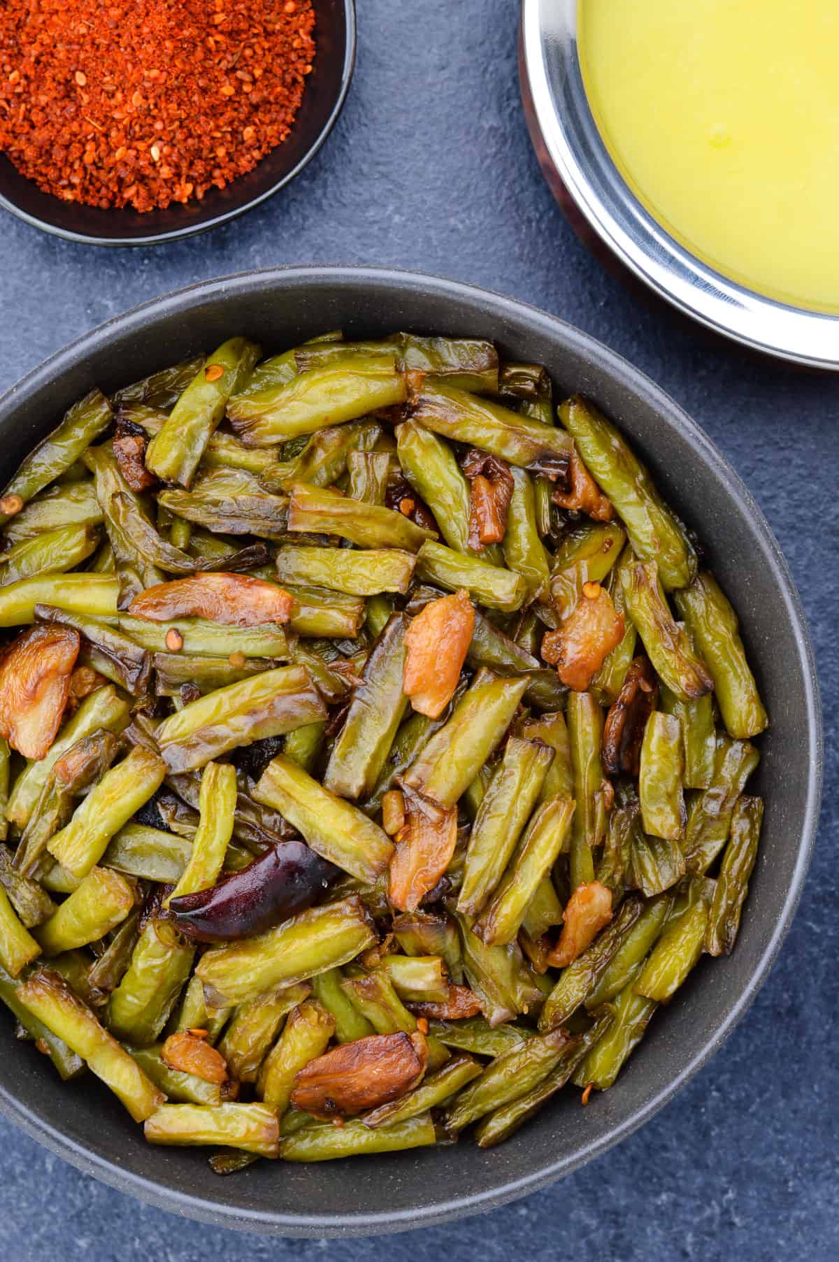 top shot of a bowl full of indian green beans stir fry, with a bowl of dal and red garlic chutney in the background.