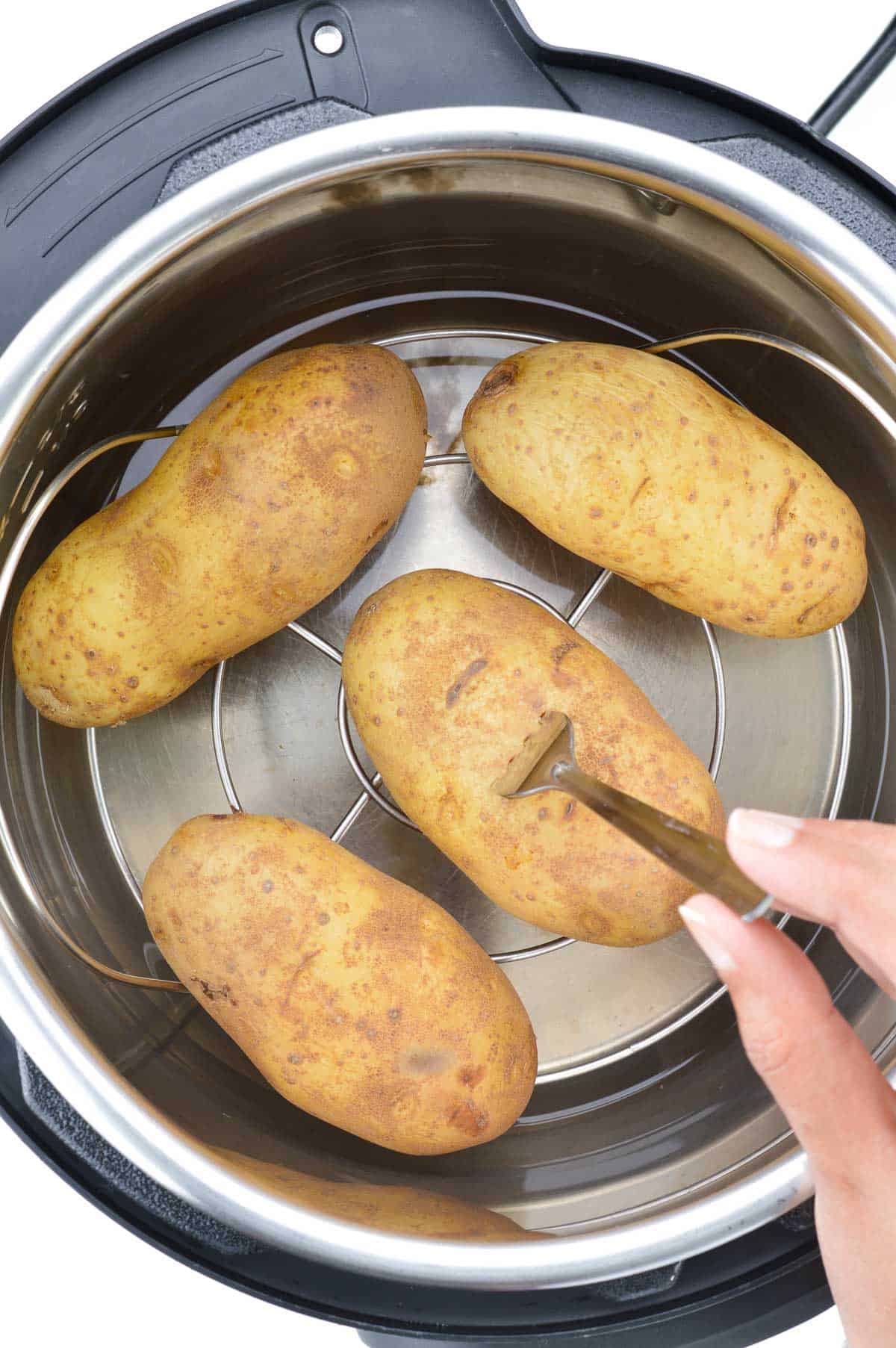 a close up of fork-tender boiled potatoes placed on a trivet inside the instant pot.