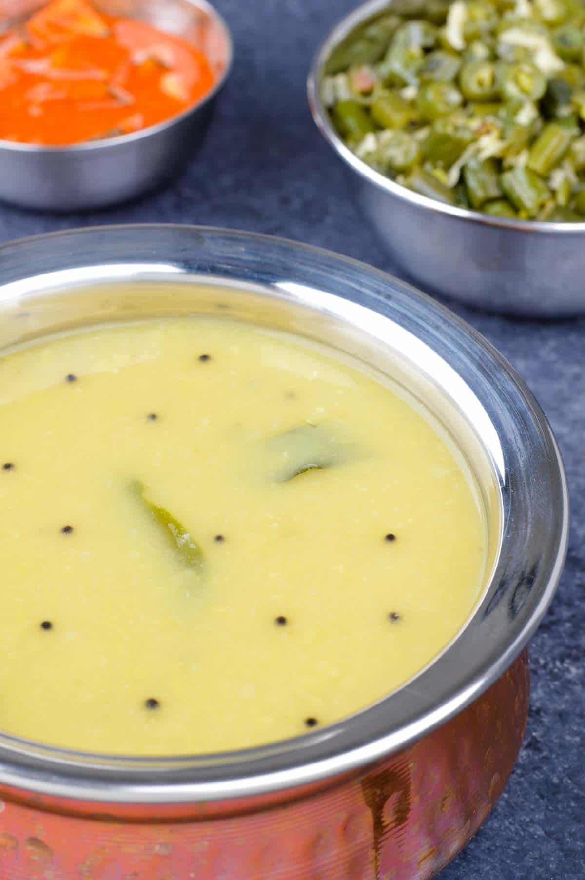 close up shot of a serving kadai full of dalitoy, with a bowl of beans upkari in the background, along with a small bowl of pickle.