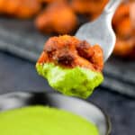 close up shot of a boneless tandoori chicken bite dipped in green chutney.