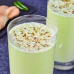 close up shot of a glass full of masala chaas, with another glass of chaas in the background, along with some whole ginger and chillies on the side.