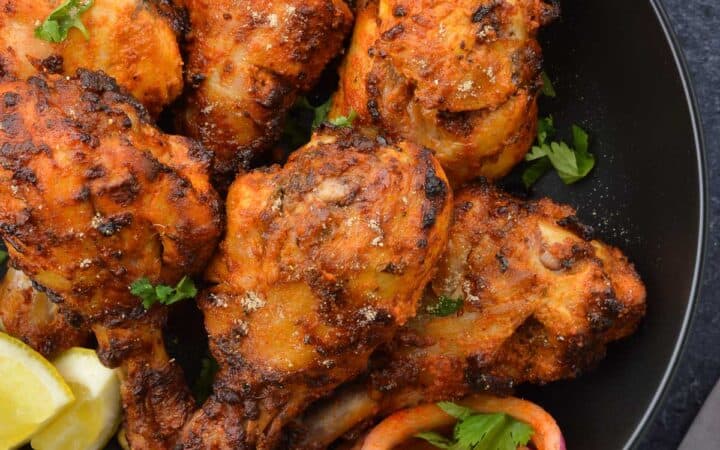 air fried tandoori chicken drumsticks in a bowl, along with laccha pyaaz, a couple lemon wedges & chopped coriander leaves.